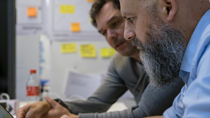 Two men sitting in a conference room have a discussion as they look at a laptop.