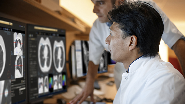 Two medical professionals look at diagnostic results on a series of monitors